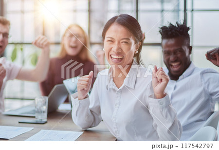 group of different business people celebrating victory while sitting at table in modern office group of different business people celebrating victory while sitting at table in modern office 117542797