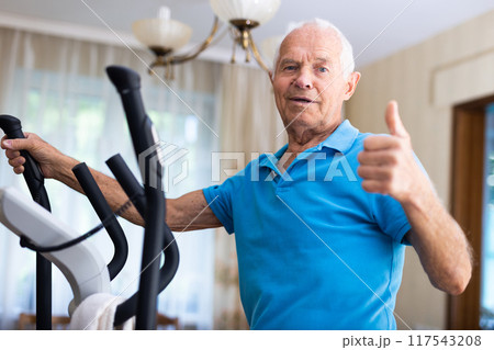 Mature man exercising on an elliptical machine and showing thumb up 117543208