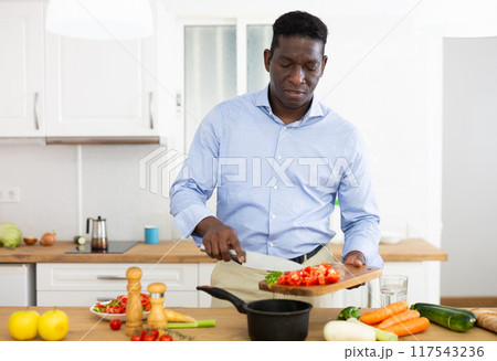 Smiling african american man eating apple in home kitchen 117543236