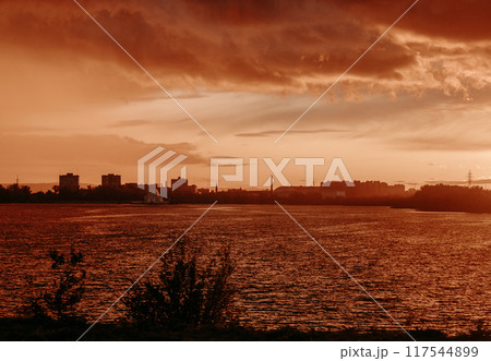 silhouette of the city at sunset near the river, against a red-orange background 117544899