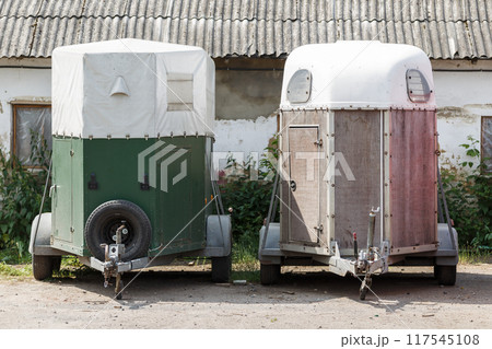 Two horse trailers parked outside a rustic barn on a sunny day Two horse trailers parked outside a rustic barn on a sunny day 117545108