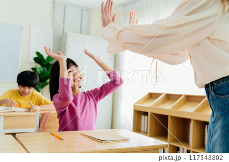 Joyful Asian primary student celebrating achievement with teacher through energetic high-five Joyful Asian primary student celebrating achievement with teacher through energetic high-five 117548802