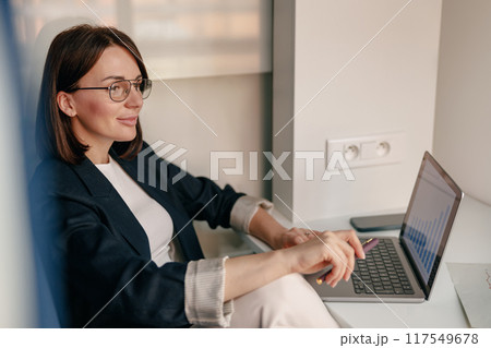 Confident businesswoman working on laptop in a modern office, showcasing dedication and efficiency Confident businesswoman working on laptop in a modern office, showcasing dedication and efficiency 117549678