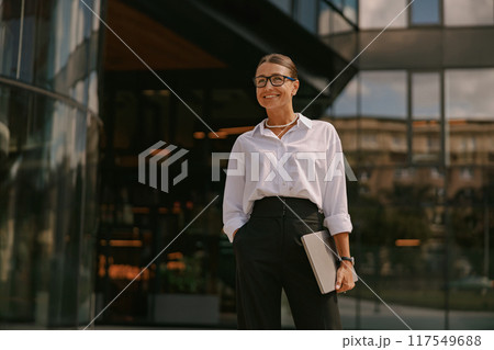 A confident, successful businesswoman stands outside a modern office building, radiating elegance A confident, successful businesswoman stands outside a modern office building, radiating elegance 117549688