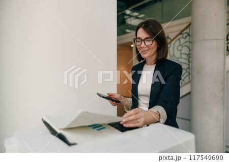 Professional Businesswoman Using Smartphone and Organizing Documents in Office with Efficiency Professional Businesswoman Using Smartphone and Organizing Documents in Office with Efficiency 117549690
