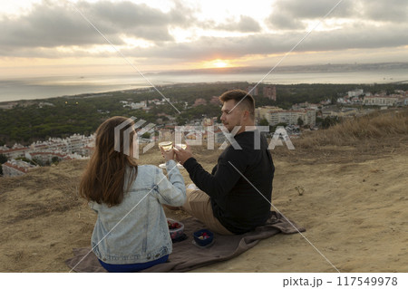 Loving couple having romantic picnic with wine at sunset overlooking city 117549978