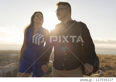 Loving couple holding hands and walking on mountaintop at sunset 117550117
