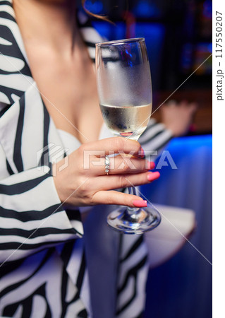 A woman holds a cocktail in her hand, with her fingers wrapped around the glass A woman holds a cocktail in her hand, with her fingers wrapped around the glass 117550207