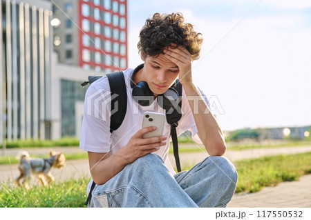 Upset sad unhappy young male guy reading message on smartphone, outdoor 117550532