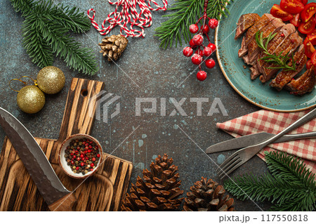 Festive Christmas dinner boarder background with space for text with roasted duck breast fillet with golden crispy skin and tomato salad, Xmas decorations with fir tree, cones, red berries. Festive Christmas dinner boarder background with space for text with roasted duck breast fillet with golden crispy skin and tomato salad, Xmas decorations with fir tree, cones, red berries. 117550818