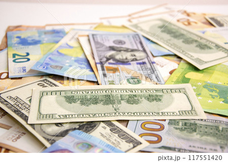A close-up photograph showing a collection of US Dollar and Euro banknotes strewn across a white surface 117551420
