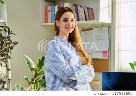Portrait of smiling female teenager looking at camera with crossed arms in home Portrait of smiling female teenager looking at camera with crossed arms in home 117551693