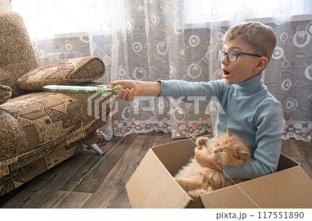 A small child, a boy, plays a pirate with a cat sitting in a box. Children's games in the children's room. Real friendship 117551890
