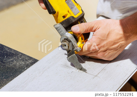 Worker is using multitool to make hole in laminate panel for an outlet 117552291