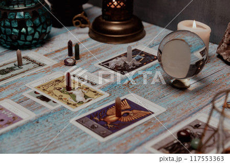 A tarot card reading session depicted with candles, crystals, and mystical accessories on a rustic wooden table. 117553363