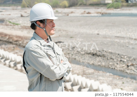 土木業・河川工事・建設現場に立つヘルメットを被った作業着姿のアジア人男性作業員 117554044