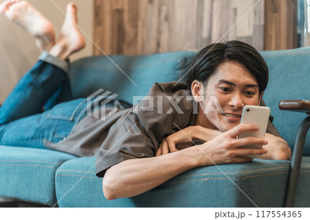 家でくつろぎながらスマホ・スマートフォンをいじる若い男性(SNS・動画・ネットショッピング) 家でくつろぎながらスマホ・スマートフォンをいじる若い男性(SNS・動画・ネットショッピング) 117554365