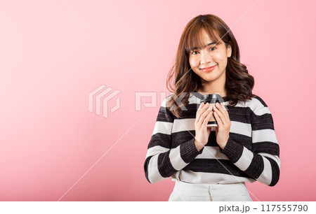 Portrait Asian Thai beautiful happy young woman standing smiling holding take away coffee paper cup, studio shot isolated on pink background with copy space, coffee break 117555790