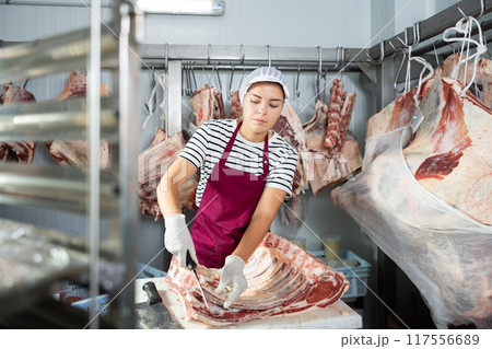 Female employee of local butcher shop divides large huge piece of meat with knife Female employee of local butcher shop divides large huge piece of meat with knife 117556689