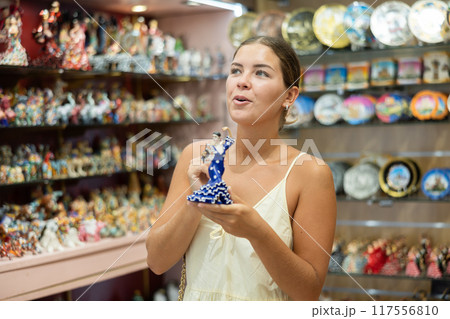 Happy young woman choosing statue of Spanish dancer among various souvenirs in gift shop in Barcelona 117556810
