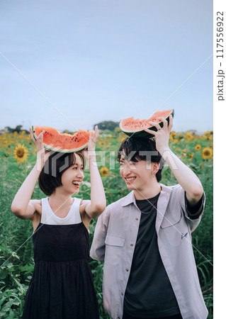 スイカを持ってひまわり畑で前撮りするカップル スイカを持ってひまわり畑で前撮りするカップル 117556922