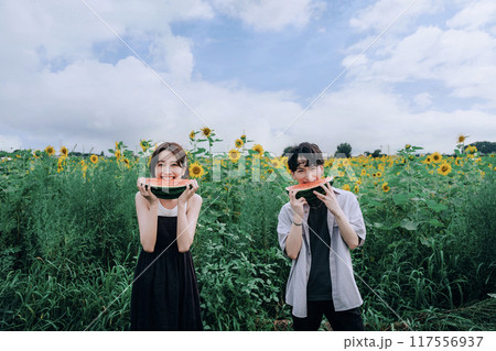 スイカを持ってひまわり畑で前撮りするカップル 117556937