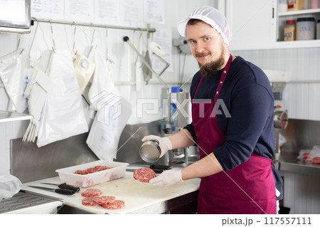 Bearded worker pressing ground beef hamburger patties in butcher shop Bearded worker pressing ground beef hamburger patties in butcher shop 117557111