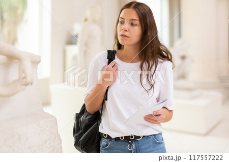 Focused girl visitor looks with interest at the sculpture in the museum hall Focused girl visitor looks with interest at the sculpture in the museum hall 117557222