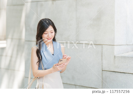 オフィス街でスマートフォンを操作しているビジネスウーマン オフィス街でスマートフォンを操作しているビジネスウーマン 117557256