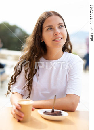 Portrait of a positive girl sitting at a table with a cup of delicious coffee 117557261