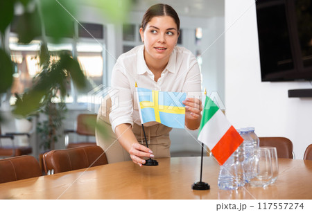 Employee of delegation prepares negotiating table - sets up flag of Swede and Finland Employee of delegation prepares negotiating table - sets up flag of Swede and Finland 117557274