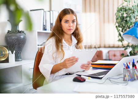 Focused young business woman working at office desk Focused young business woman working at office desk 117557380