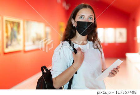 Young girl in a protective mask visits an exhibition of paintings in a museum Young girl in a protective mask visits an exhibition of paintings in a museum 117557409