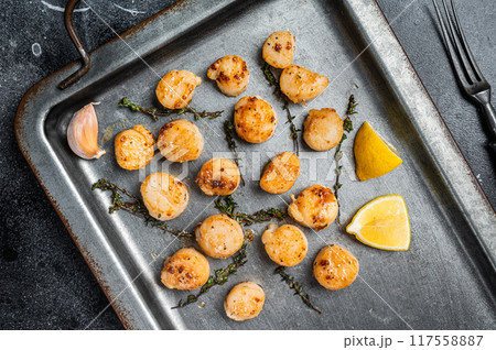 Scallops poached in a butter and garlic Sauce in a steel tray with thyme. Black background. Top view Scallops poached in a butter and garlic Sauce in a steel tray with thyme. Black background. Top view 117558887