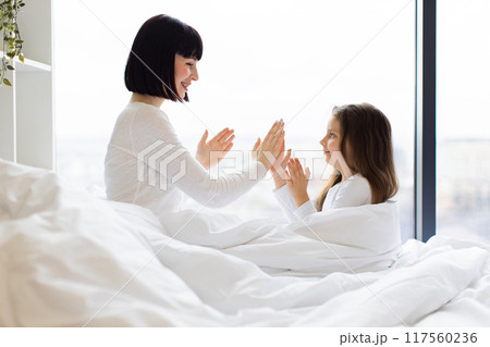 Mother and daughter playing clapping game in bed Mother and daughter playing clapping game in bed 117560236