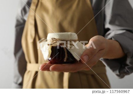 Glass jar with fig jam in hand on light background, close up Glass jar with fig jam in hand on light background, close up 117560967