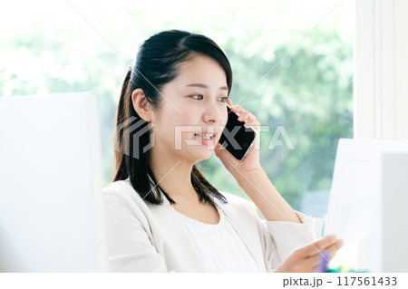 資料を手にスマホで通話する女性 117561433