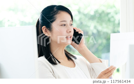 資料を手にスマホで通話する女性 資料を手にスマホで通話する女性 117561434