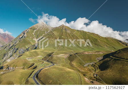 A Serene Mountain Landscape featuring a Winding Road that stretches under a Clear Blue Sky A Serene Mountain Landscape featuring a Winding Road that stretches under a Clear Blue Sky 117562927