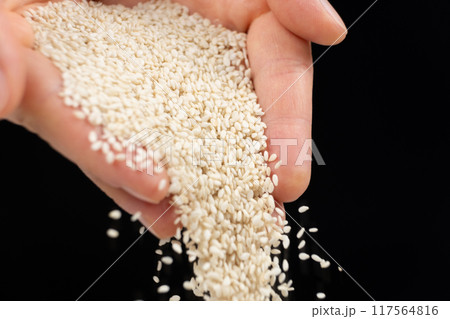 Hands pouring white sesame seeds on black background 117564816