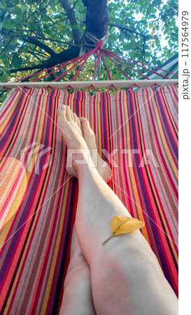 Woman relaxes in red striped hammock in her garden. Close-up selfies of legs 117564979