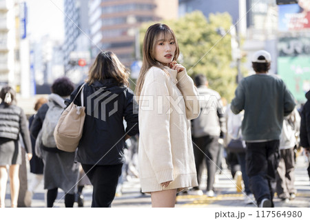 混雑した都会の交差点を背景に立つカメラ目線の20代の女性　 117564980