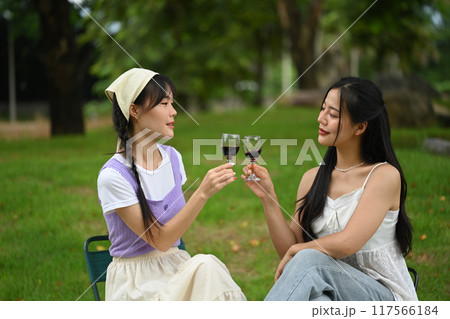 Happy asian women friends having fun outdoor and toasting with wine glasses at picnic Happy asian women friends having fun outdoor and toasting with wine glasses at picnic 117566184