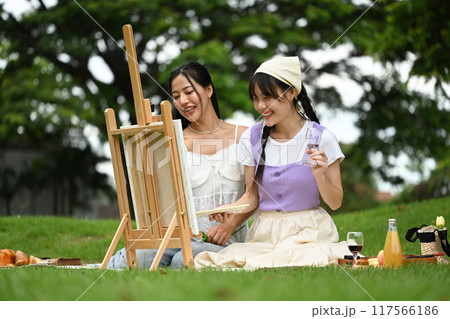 Two young asian women painting on easel with watercolors in a park Two young asian women painting on easel with watercolors in a park 117566186