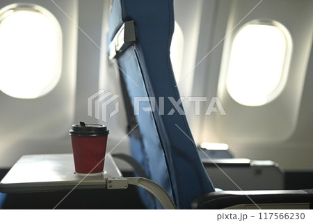 A red disposable coffee cup on airplane tray table in front of a blue chair 117566230
