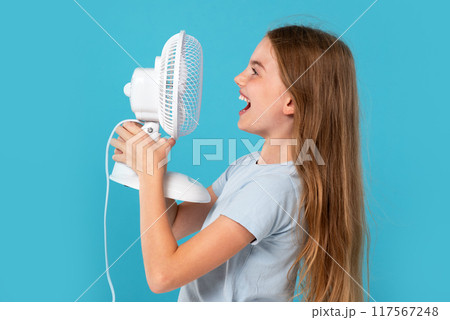 Child girl enjoying cool air. Child and fan on blue background. Room temperature regulation Child girl enjoying cool air. Child and fan on blue background. Room temperature regulation 117567248
