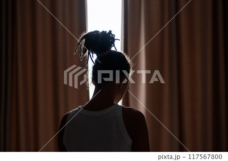 Females silhouette with bun hairstyle standing in front of window in dimly lit room. Females silhouette with bun hairstyle standing in front of window in dimly lit room. 117567800