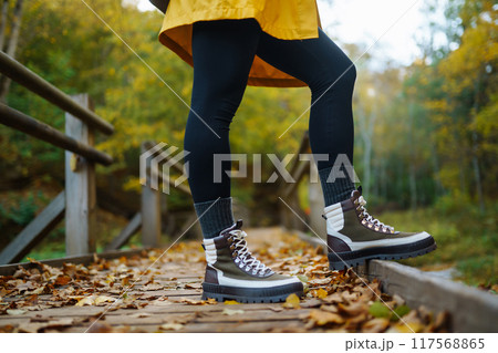 Women's feet in boots go along a wooden walking path in the autumn forest. Women's feet in boots go along a wooden walking path in the autumn forest. 117568865