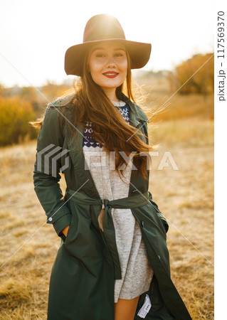 Beautiful stylish girl walks in the autumn park. The girl is dressed in a green coat and a red hat. Beautiful stylish girl walks in the autumn park. The girl is dressed in a green coat and a red hat. 117569370