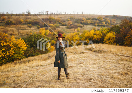 Beautiful stylish girl walks in the autumn park. The girl is dressed in a green coat and a red hat. Beautiful stylish girl walks in the autumn park. The girl is dressed in a green coat and a red hat. 117569377